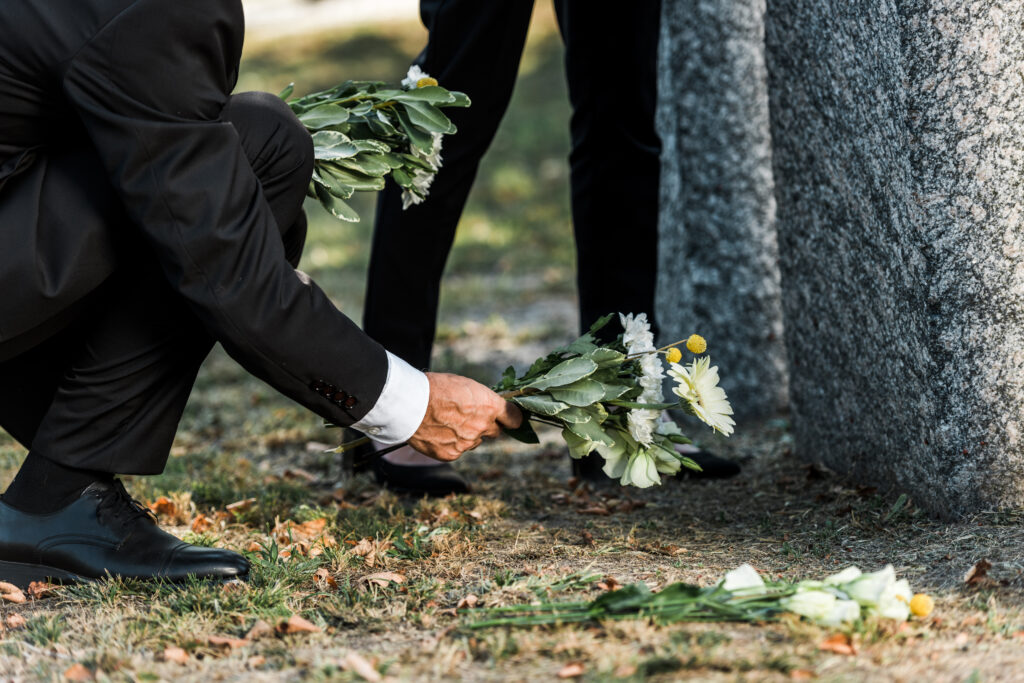 Cropped view of senior man putting flowers near tombstones and woman.